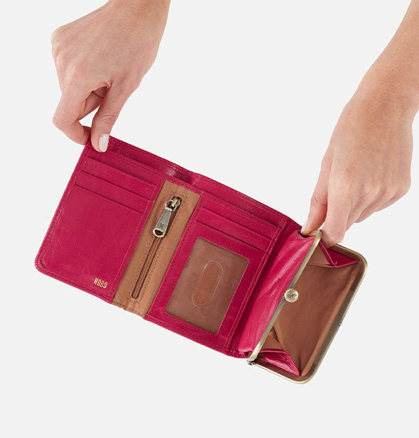 Model's hands hold open a fuchsia leather wallet to reveal pockets inside accented with brown lining and gold hardware