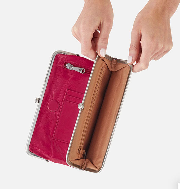 Model holds open a section of a fuchsia leather wallet to show brown interior with additional zip pocket