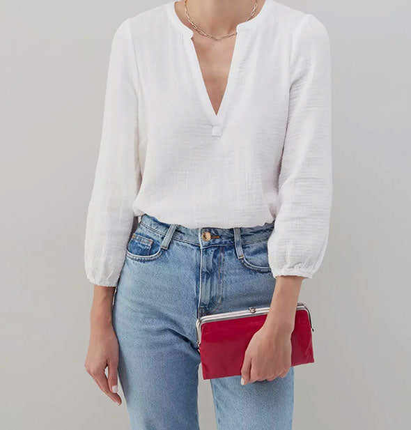 Model wearing jeans and a white shirt holds a fuchsia leather wallet with silver-toned frame hardware for size reference
