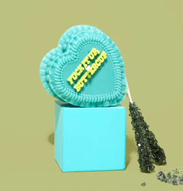 Fuck It Up, Buttercup heart-shaped cake candle is staged on a teal cube with rock candy