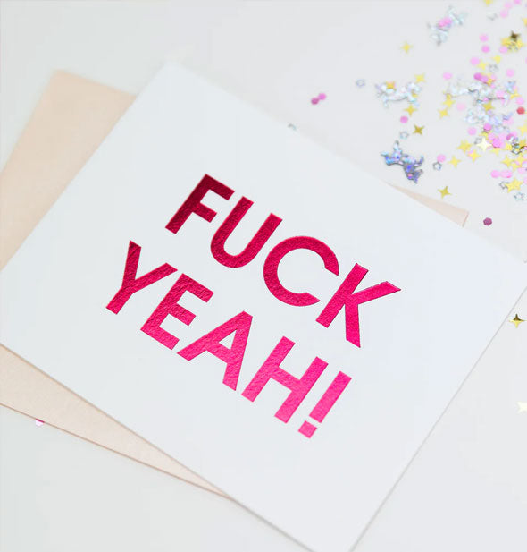 Fuck Yeah! greeting card rests on top of a pastel pink envelope next to a sprinkling of glitter