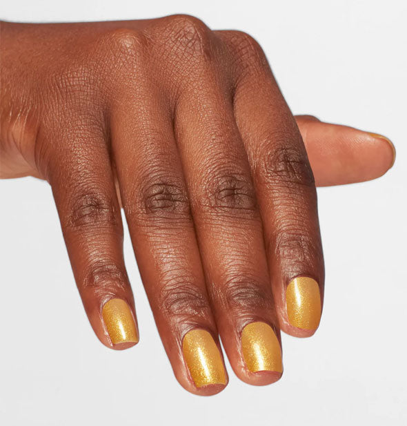 Model's hand wears a shimmery shade of orangey-gold nail polish