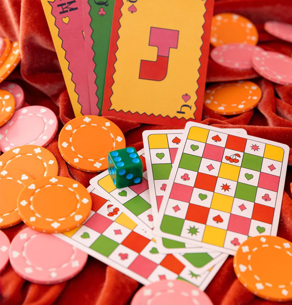 Two spreads of colorful playing cards on bunched-up red velvet with poker chips and a die