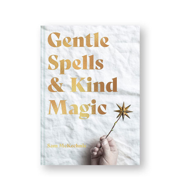 Cover of Gentle Spells & Kind Magic features large metallic gold lettering and image of a hand holding a gold, star-topped wand against a crinkled white backdrop