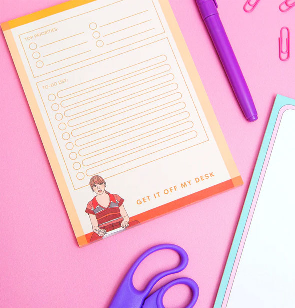Taylor Swift Get It Off My Desk notepad on a pink surface with other stationery supplies