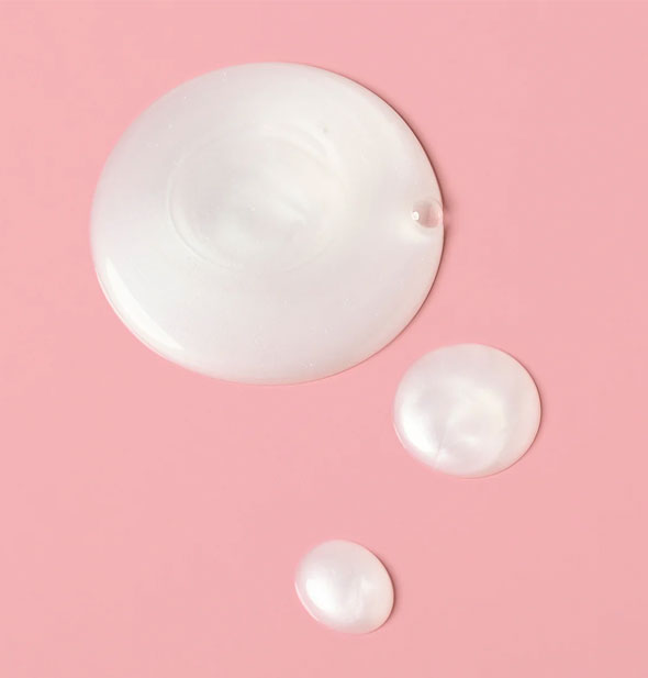 Closeup of white, slightly pearlescent droplets of Verb Ghost Shampoo on a pink surface