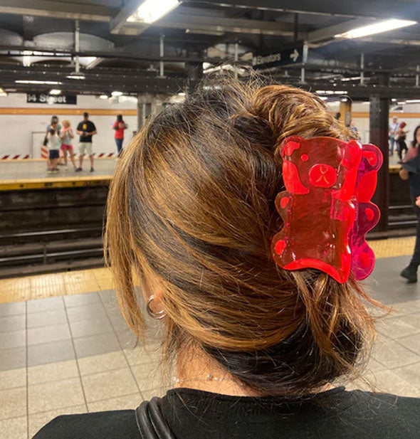 Model wears a large red gummy bear hair clip in a twist updo against a subway backdrop