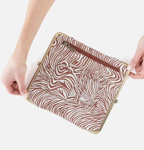 Model's hands hold open a brown and white zebra print wallet with brass hardware, interior zip pockets, and a brown zipper pocket