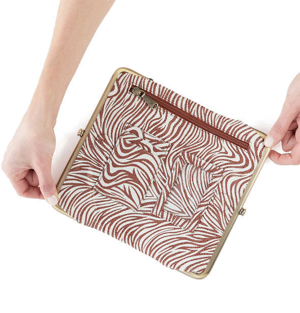 Model's hands hold open a brown and white zebra print wallet with brass hardware, interior zip pockets, and a brown zipper pocket