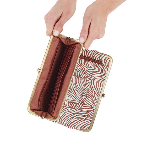 Model's hands hold open a section of brown and white zebra print wallet with brown lining and brass frame hardware