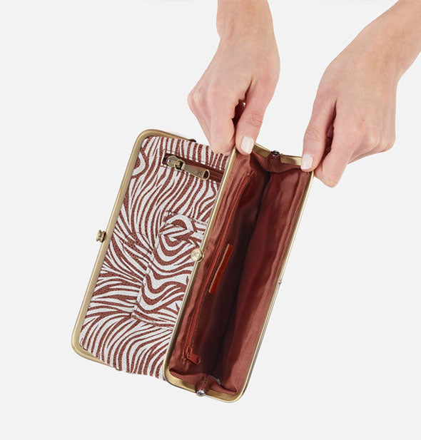 Model's hands hold open a section of brown and white zebra print wallet with brown lining and brass frame hardware