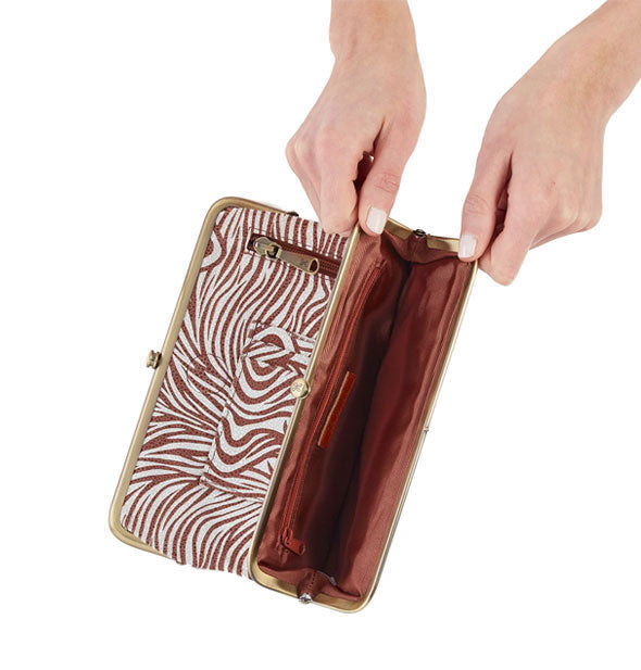 Model's hands hold open a section of brown and white zebra print wallet with brown lining and brass frame hardware