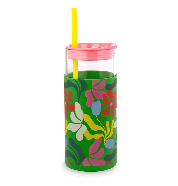 Glass drink tumbler with green sleeve patterned with colorful abstract florals, a pink lid, and yellow straw