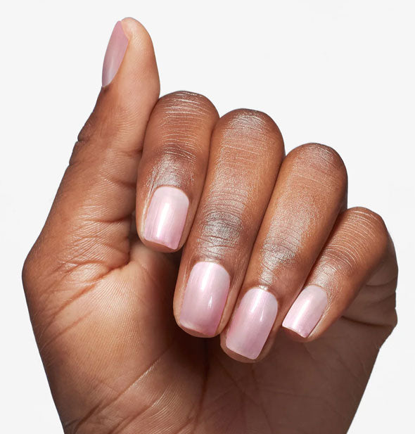 Model's hand wears a pearlescent pink shade of nail polish