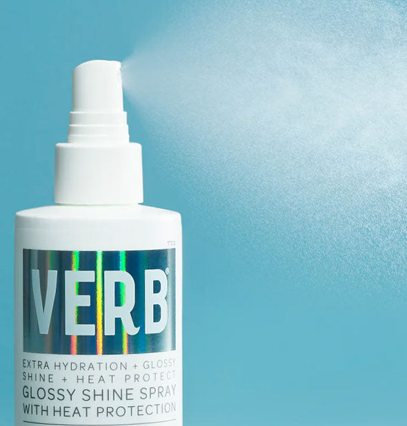 A fine mist of product is dispensed from a bottle of Verb Glossy Shine Spray against a blue backdrop