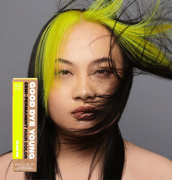 Model wears neon yellow bangs in dark hair; box of Good Dye Young Semi-Permanent Hair Color in shade Glow On is inset at bottom left