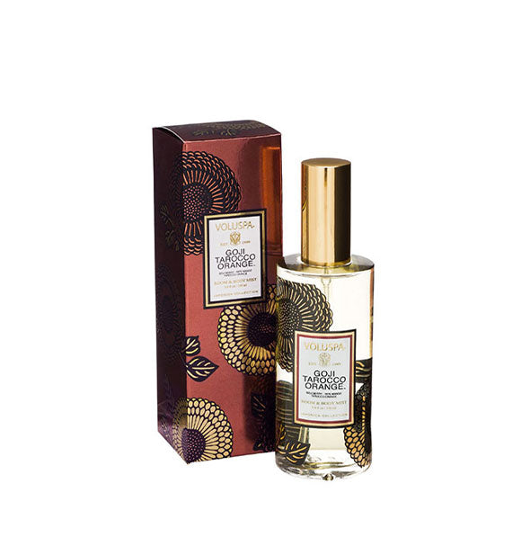 Floral-patterned clear glass bottle of Voluspa Goji Tarocco Orange Room & Body Mist next to metallic red gift box with black and gold floral pattern