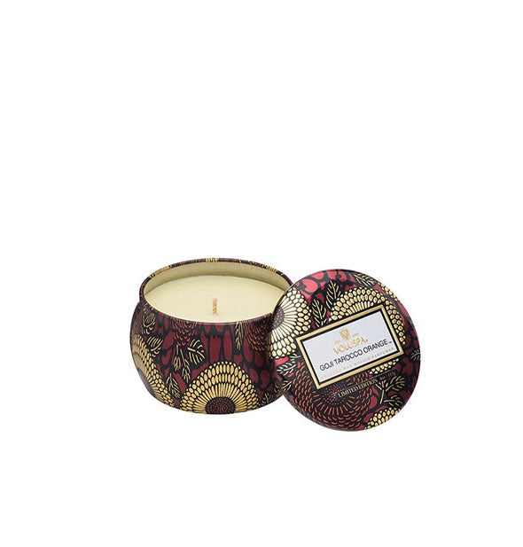 A small unlit candle inside a rounded tin with red and gold metallic floral design and matching lid set to the side