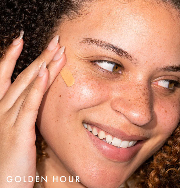 Model applies Coola Rosilliance Tinted Moisturizer Sunscreen in shade Golden Hour to cheek