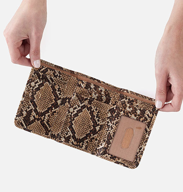 Model's hands hold open a small gold snakeskin print trifold wallet to show storage slots inside