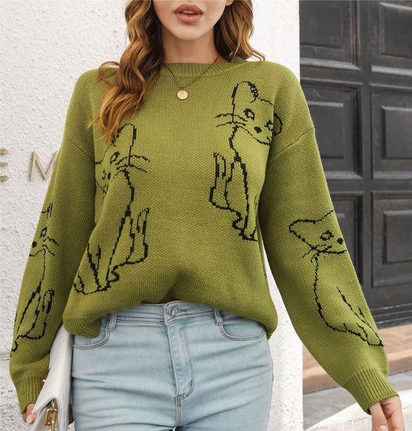 Model wears an olive green jacquard sweater with black outlined cats design