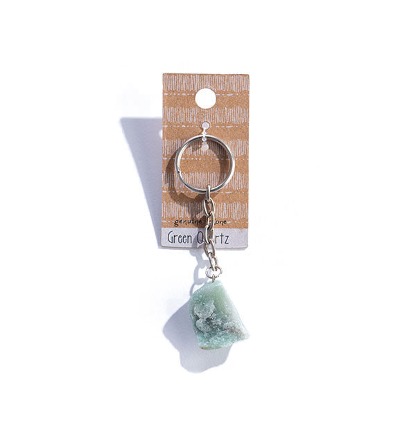 A chunk of green quartz is attached to a metal keychain which hangs from a decorative rectangular card.