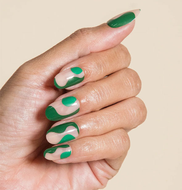 Model's hand wears press-on nails with a natural base and abstract shapes in two shades of green