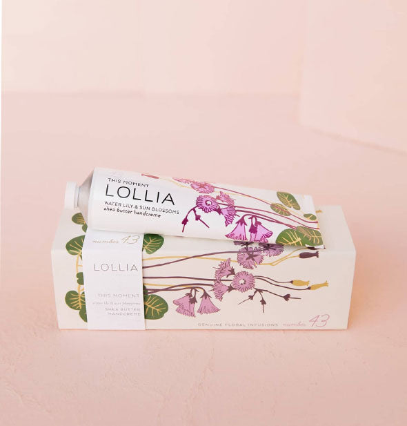 White tube and box of Lollia This Moment Water Lily & Sun Blossoms Shea Butter Handcreme with purple, green, and gold florals and leaves designs