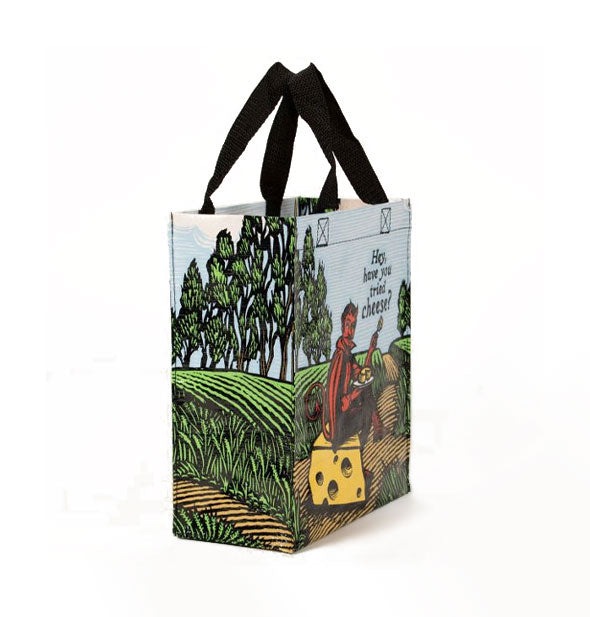 Tote bag with black handles features an all-over pastoral scene in the middle of which is a red devil sitting on a block of Swiss asking, "Hey, have you tried cheese?"