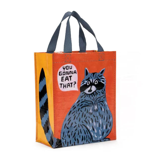 Two-tone orange tote bag with blue top handles features illustration of a blue-gray raccoon saying, "You gonna eat that?"