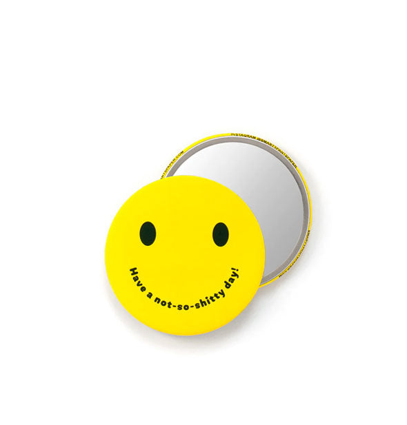 Two views of a round pocket mirror with bright yellow smiley face on one side that says, "Have a not-so-shitty day!" where the mouth should be