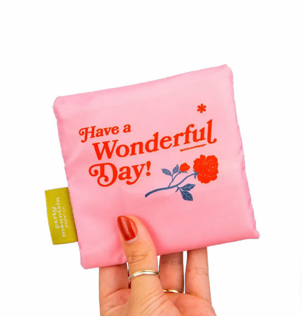 Model's hand holds a pink Have a Wonderful Day shopping bag that's been folded into a square