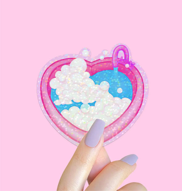 Model's hand holds a sticker designed as a pink heart-shaped bath tub with water running from its faucet and a mound of white bubbles