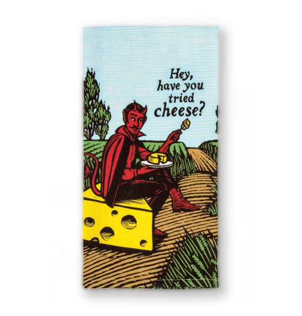 Dish towel depicting a red devil sitting on a large slice of yellow cheese in a pastoral setting holding a plate and fork with cheese on them says, "Hey have you tried cheese?"