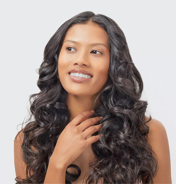 Smiling model gently touches shiny, voluminous curls in very long hair