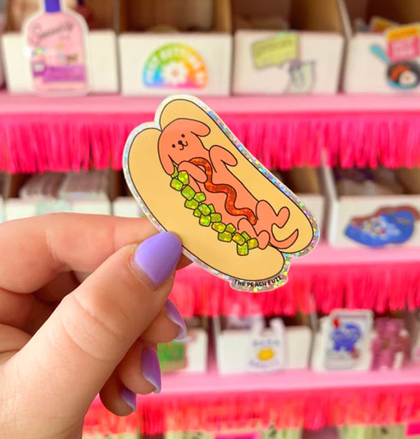 Model's hand holds a hot dog sticker in front of a shop display