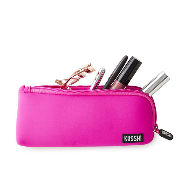 Rectangular hot pink KUSSHI pouch is shown unzipped with cosmetic items emerging from inside