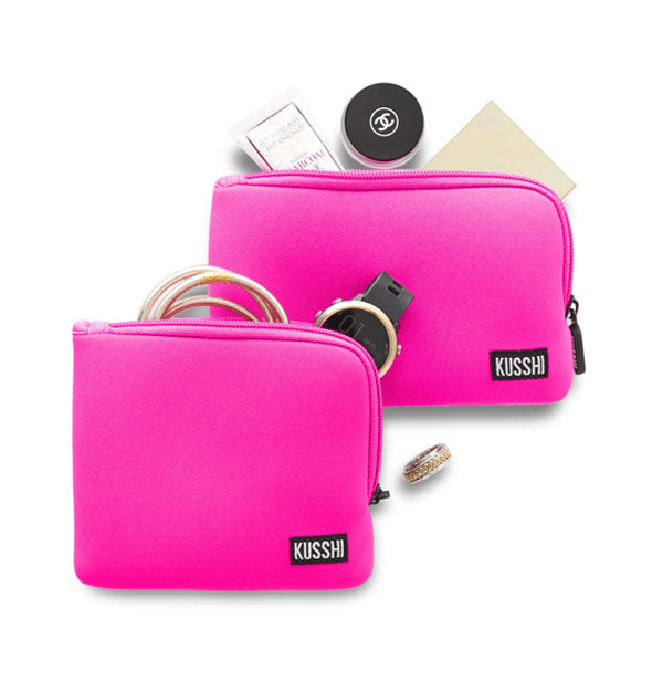 Two hot pink KUSSHI pouches, one square and one rectangular, with personal items appearing to fall out of each