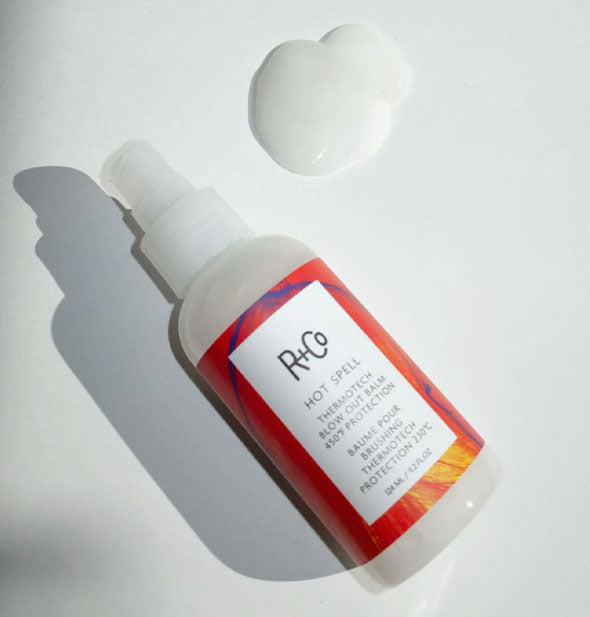 Bottle of R+Co Hot Spell on its side next to a large droplet of dispensed product