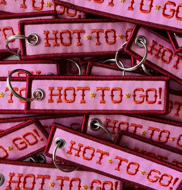 A pile of rectangular pink cloth tabs with red embroidered edges and lettering that says, "Hot to go!" accented with yellow stars