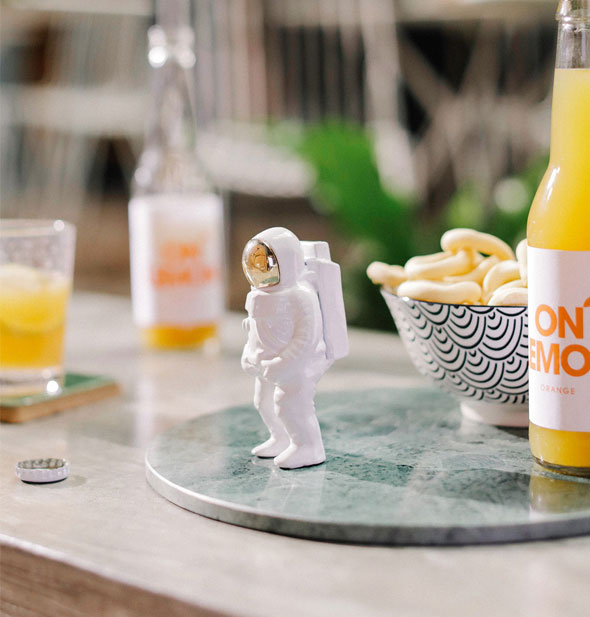 White astronaut figurine bottle opener is staged with bottled lemon drinks and a bowl of snacks