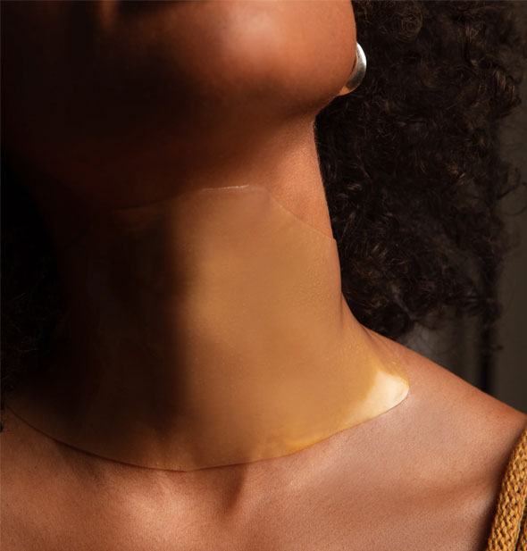 Model wears a gold-colored sheet mask on neck