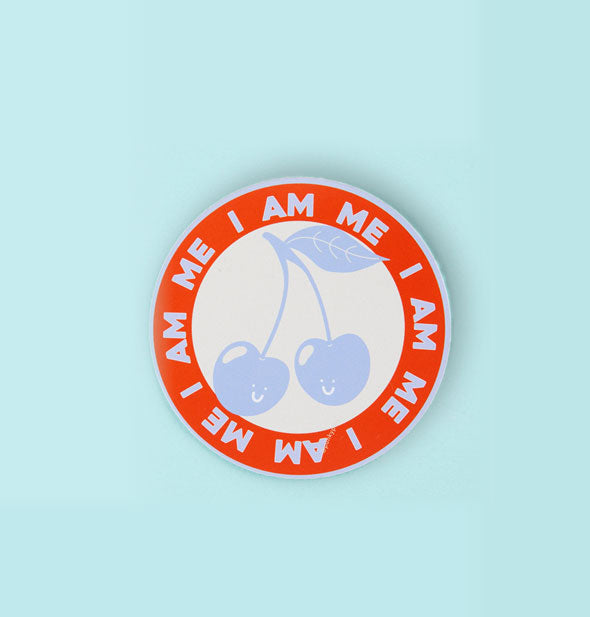Round sticker says, "I Am Me" in repeating blue lettering in an outer red ring that encircles a pair of smiling blue cherries