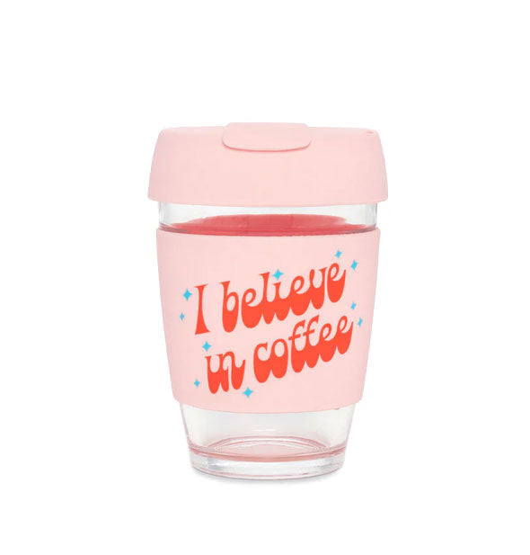 Clear glass drink tumbler with light pink lid and central band that says, "I believe in coffee" in retro-style red lettering accented with blue stars