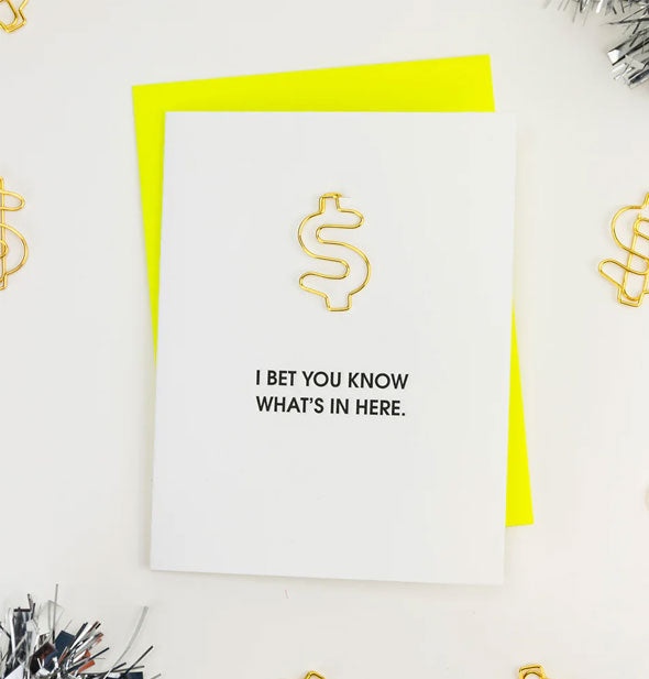 I Bet You Know What's In Here greeting card with neon yellow envelope staged with other money symbol paper clips, like the one on it, and silver tinsel
