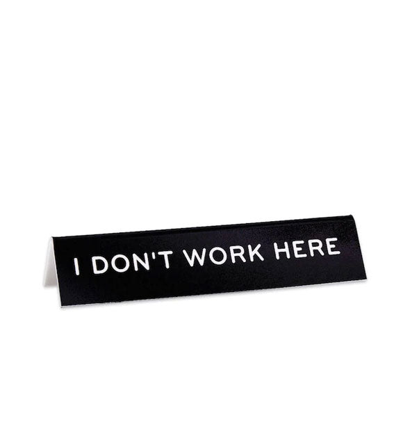 Black rectangular desk sign says, "I don't work here" in white lettering