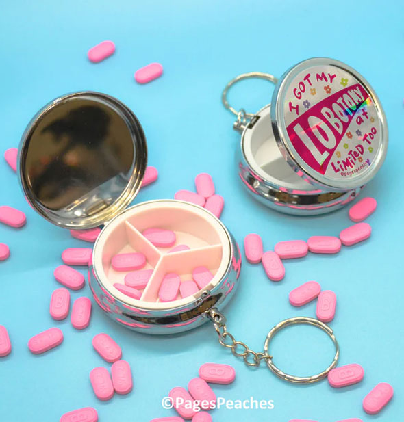 Lobotomy keychain pill cases shown open with 3-way divider interior shown and small pink tablets scattered throughout on a blue surface