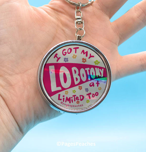 Model's hand holds an I Got My Lobotomy at Limited Too pill case keychain