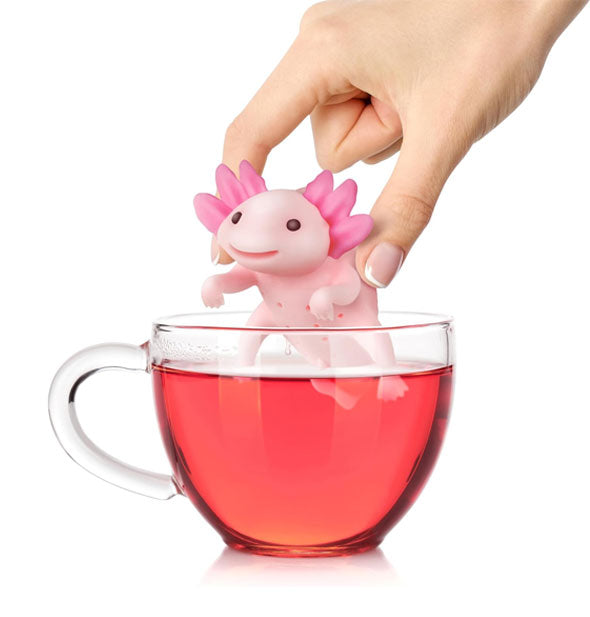 Model's hand lifts a pink axolotl infuser from a mug of tea