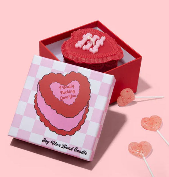 I Really Fucking Love You cake candle in a red box with pink and white checkered lid removed is staged with heart-shaped lollipops scattered about